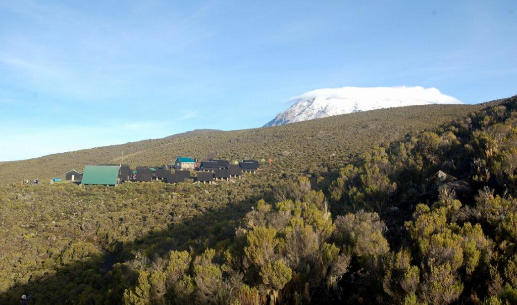 A campsite along the Marangu Route with the snow-capped summit of Mount Kilimanjaro in the background.