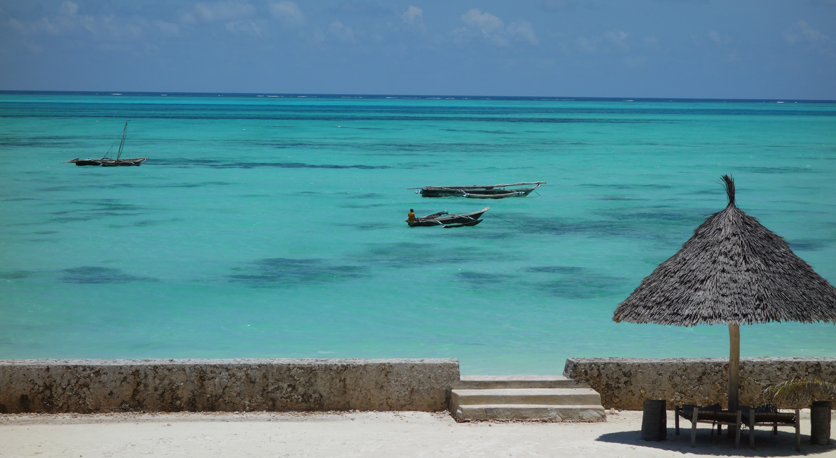 The Indian Ocean stretches off the coast of Zanzibar, where three fishing boats drift near a small thatched pavilion. The Indian Ocean stretches off the coast of Zanzibar, where three fishing boats drift near a small thatched pavilion.