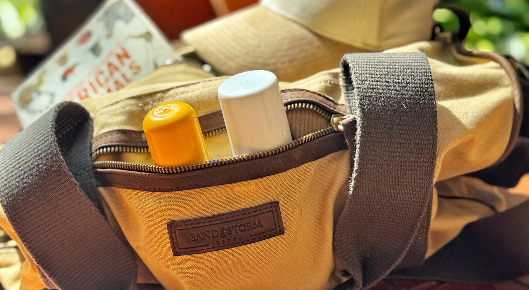 Eine SandstormTasche gefüllt mit Sonnencreme, Insektenschutzmittel, einem Buch und einem Hut. Eine SandstormTasche gefüllt mit Sonnencreme, Insektenschutzmittel, einem Buch und einem Hut.