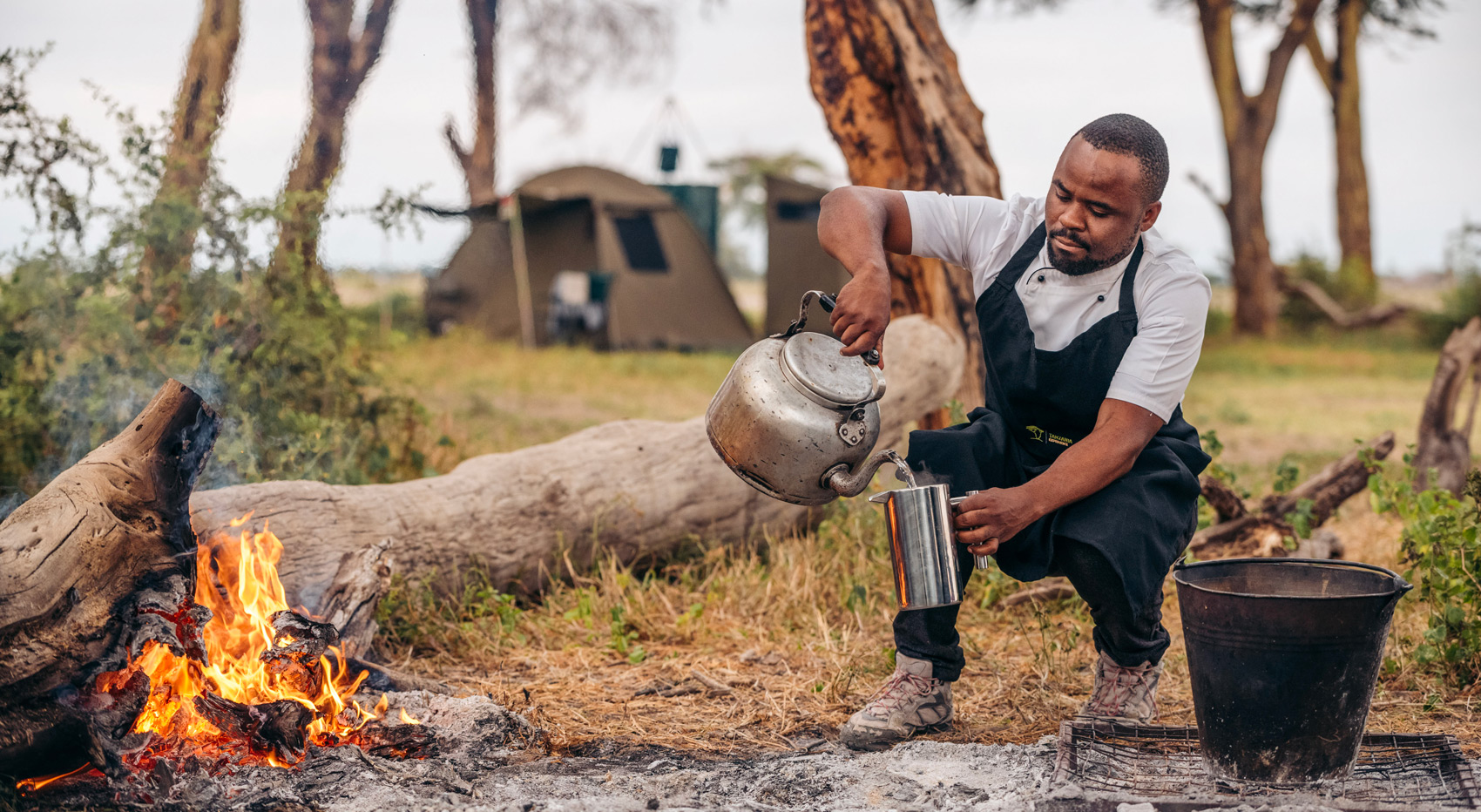 A camp staff member making coffee with water heated on open fire. A camp staff member making coffee with water heated on open fire.