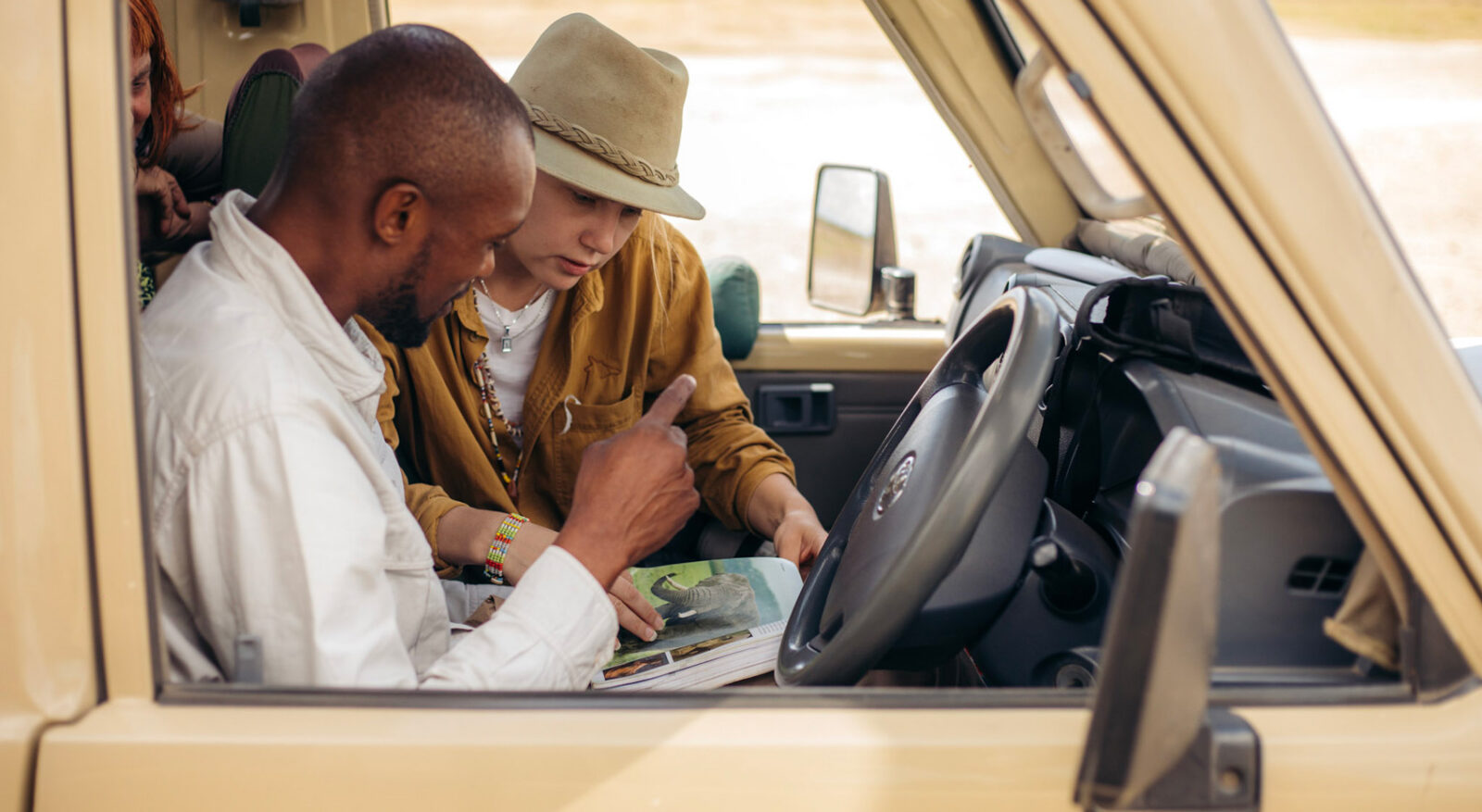A guide and a guest in a vehicle looking at a wildlife book. A guide and a guest in a vehicle looking at a wildlife book.